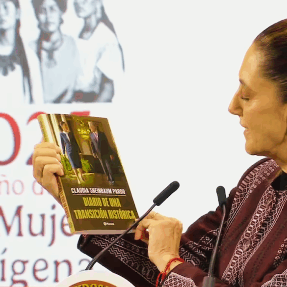 La presidenta Claudia Sheinbaum sostiene y muestra su libro Diario de una transición histórica durante su presentación en Palacio Nacional. Al fondo se observa un cartel con la leyenda “2025, Año de la Mujer Indígena”.