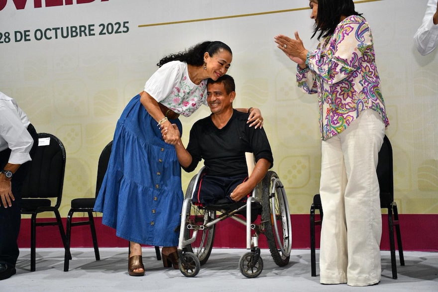 Aurora Raleigh abraza a un beneficiario en silla de ruedas durante la entrega de apoyos.