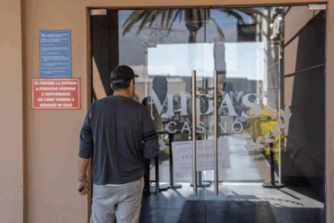 Hombre observa la puerta clausurada del casino Midas con aviso de suspensión visible.