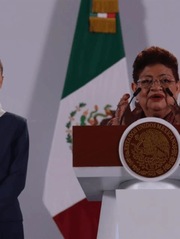Claudia Sheinbaum observa mientras Ernestina Godoy habla en el podio presidencial durante anuncio en Palacio Nacional.