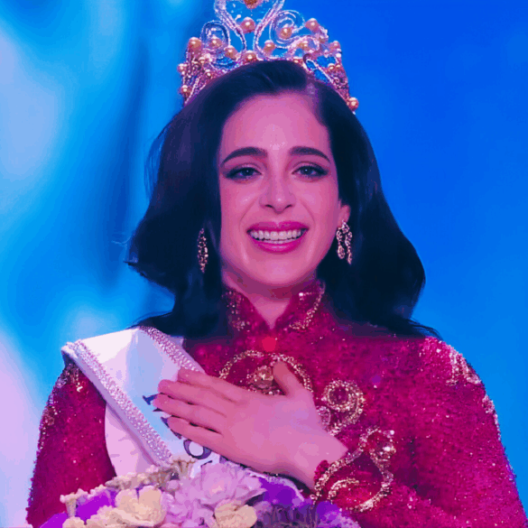 Mujer coronada con traje rojo y corona dorada, sonriendo emocionada en el escenario de Miss Universe 2025.