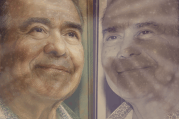 Retrato póstumo de Gustavo Rosario Torres, con expresión serena y guayabera blanca, fondo cálido y luz tenue.