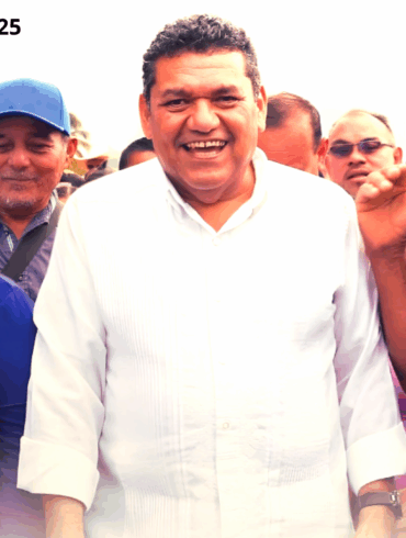 Un hombre sonriente con camisa blanca camina rodeado de vecinos que también sonríen.