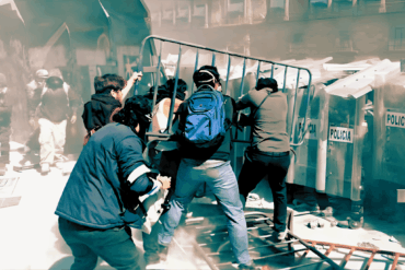 Jóvenes empujan una valla metálica contra el muro policial durante un choque en el Zócalo.