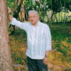 AMLO, con guayabera blanca, apoyado en un árbol dentro de un paraje arbolado del rancho donde grabó su mensaje.