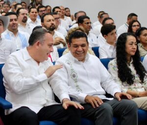 El gobernador Javier May Rodríguez conversa y ríe con el presidente del Tribunal Superior de Justicia, Carlos Efraín Reséndez Bocanegra, durante el Informe Anual de Labores 2025, acompañados por funcionarios y asistentes en el auditorio del TSJ.
