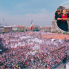 Vista aérea del Zócalo capitalino completamente lleno durante el mitin por los siete años de la 4T, con una imagen insertada de Claudia Sheinbaum saludando a simpatizantes mientras avanza entre la multitud.