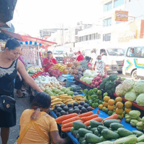 Puestos ambulantes de frutas y verduras instalados sobre la vía pública en los alrededores del mercado Pino Suárez, donde comerciantes atienden a compradores en un pasillo reducido entre mercancía y tráfico urbano.