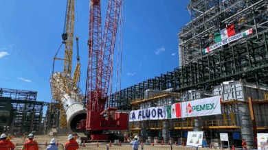 Estructura industrial de Pemex en construcción con grúas de gran tonelaje, tubería de coque en maniobra de instalación y trabajadores supervisando la obra en una planta petrolera.