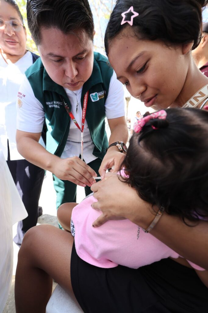 Enfermero aplica vacuna a una niña en brazos de su madre durante la Jornada de Atención al Pueblo en Pino Suárez, Comalcalco.