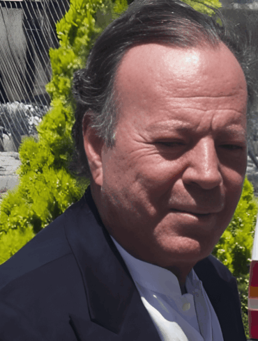 “Primer plano de un hombre de cabello canoso caminando al aire libre junto a una patrulla policial; detrás aparecen rejas metálicas y vegetación.”