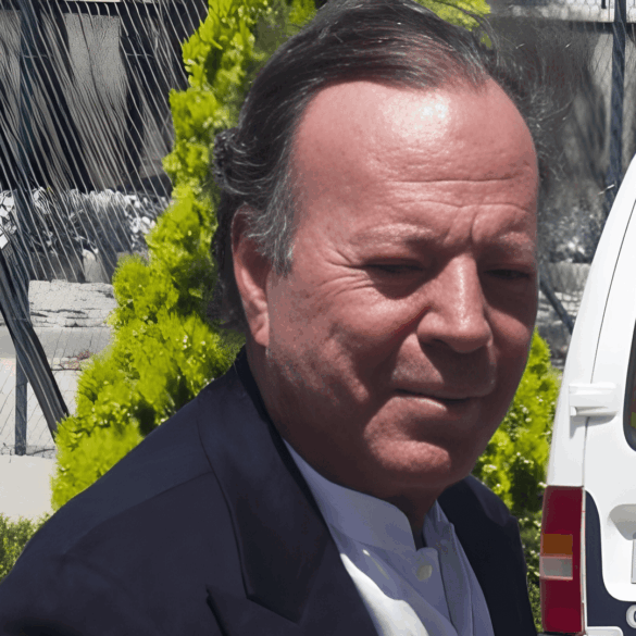 “Primer plano de un hombre de cabello canoso caminando al aire libre junto a una patrulla policial; detrás aparecen rejas metálicas y vegetación.”