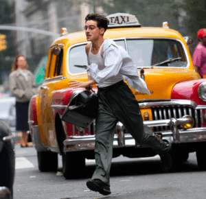 Timothée Chalamet corre despreocupado por una calle de Nueva York en una escena de Marty Supreme, caracterizado como Marty Mauser, con camisa abierta, lentes y un taxi amarillo detrás de él.