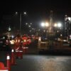 Trabajadores municipales con chalecos reflejantes realizan bacheo nocturno en el periférico de Villahermosa con conos de señalización y tráfico vehicular circulando a un costado.