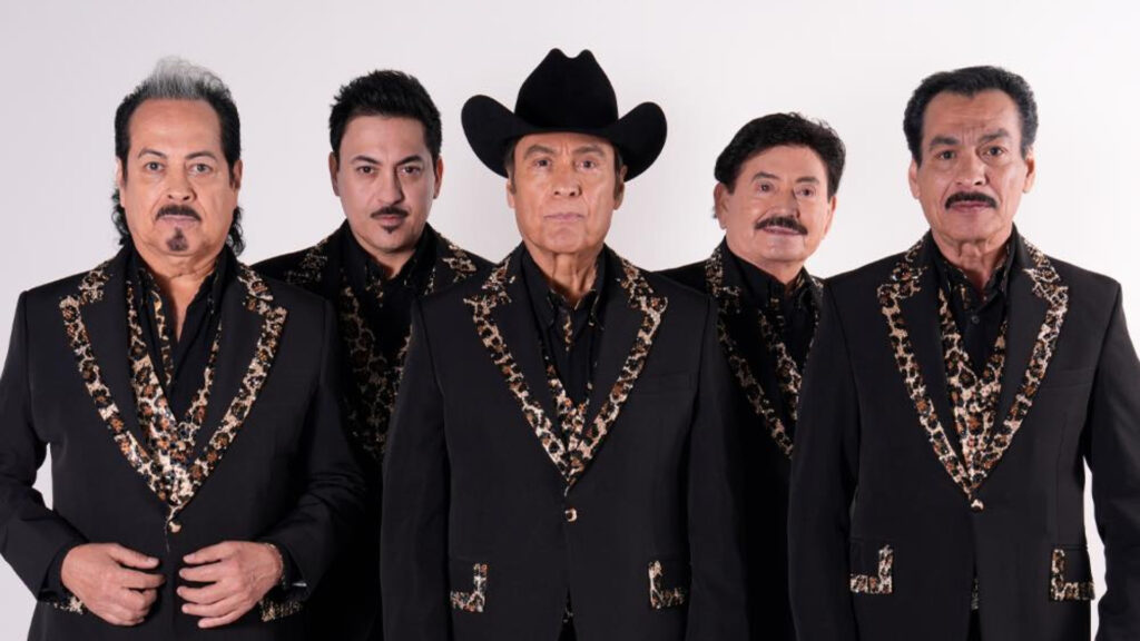 Los Tigres del Norte posan en traje negro elegante con adornos dorados, en una fotografía promocional de estudio.