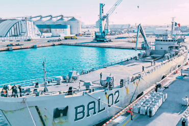 Vista general del buque BAL-02 atracado; sacos de carga apilados en muelle.