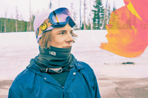 Esquiador con gorro y goggles sobre la cabeza, en una pista nevada, mira hacia la derecha con expresión seria.