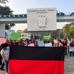 Trabajadores sindicalizados de la UJAT sosteniendo una lona rojinegra frente a la entrada de la División Académica Multidisciplinaria (DAM) en señal de inconformidad laboral.