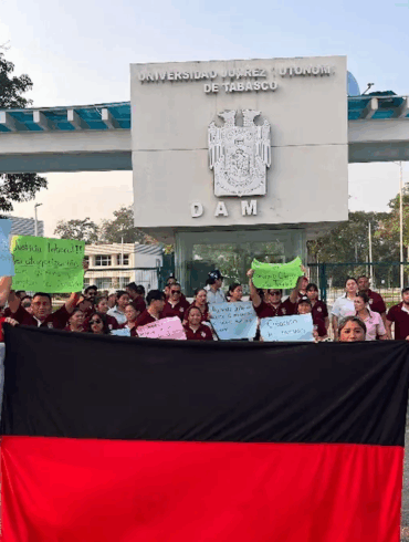 Trabajadores sindicalizados de la UJAT sosteniendo una lona rojinegra frente a la entrada de la División Académica Multidisciplinaria (DAM) en señal de inconformidad laboral.