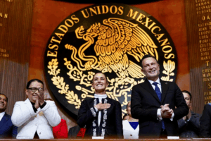 Claudia Sheinbaum junto a integrantes del gabinete y autoridades federales aplauden frente al escudo nacional durante el acto oficial.