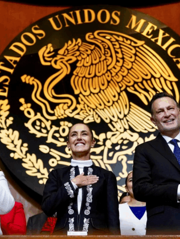 Claudia Sheinbaum junto a integrantes del gabinete y autoridades federales aplauden frente al escudo nacional durante el acto oficial.