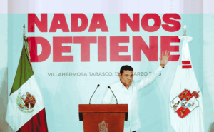 El gobernador Javier May Rodríguez levanta la mano durante su informe trimestral en Villahermosa, frente al mensaje “Nada nos detiene”.