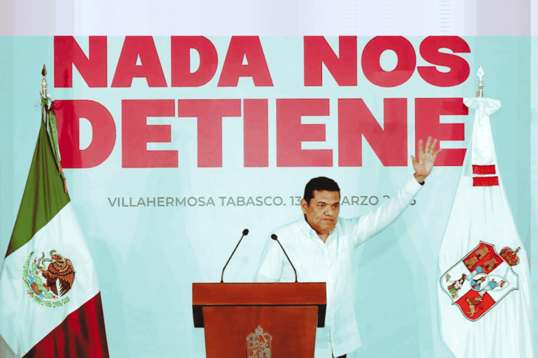 El gobernador Javier May Rodríguez levanta la mano durante su informe trimestral en Villahermosa, frente al mensaje “Nada nos detiene”.