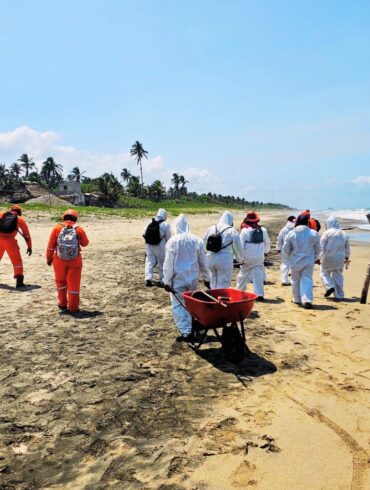 Personal con trajes protectores realiza labores de limpieza en playa afectada por hidrocarburo
