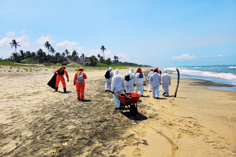 Personal con trajes protectores realiza labores de limpieza en playa afectada por hidrocarburo