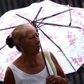 Mujer adulta mayor se protege del calor con sombrilla durante ola de calor en Tabasco