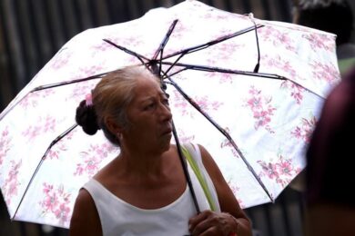 Mujer adulta mayor se protege del calor con sombrilla durante ola de calor en Tabasco