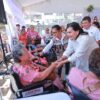 Presidenta municipal Yolanda Osuna Huerta saluda a adulta mayor en silla de ruedas durante la octava jornada de Centro +Cerca en la colonia Primero de Mayo, Villahermosa, Tabasco. Al fondo, módulos de entrega de aparatos funcionales y asistentes al evento.