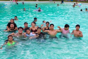 Grupo de jóvenes y familias conviviendo dentro de una alberca pública en la Ciudad Deportiva de Villahermosa durante el cierre de vacaciones