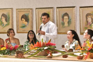 Gobernador Javier May Rodríguez habla ante las embajadoras de la Feria Tabasco 2026 en el Salón de las Flores, con retratos de Flores de Oro anteriores al fondo.
