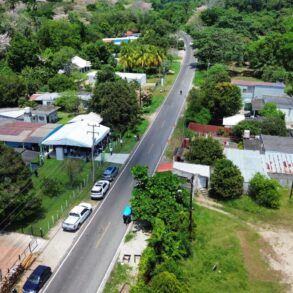 Vista aérea del camino rehabilitado que atraviesa la ranchería Sur de Comalcalco, Tabasco, flanqueado por viviendas, vegetación tropical y guayacanes en flor, parte de los 9.8 kilómetros entregados por el gobierno estatal en abril de 2026.
