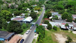 Vista aérea del camino rehabilitado que atraviesa la ranchería Sur de Comalcalco, Tabasco, flanqueado por viviendas, vegetación tropical y guayacanes en flor, parte de los 9.8 kilómetros entregados por el gobierno estatal en abril de 2026.