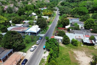 Vista aérea del camino rehabilitado que atraviesa la ranchería Sur de Comalcalco, Tabasco, flanqueado por viviendas, vegetación tropical y guayacanes en flor, parte de los 9.8 kilómetros entregados por el gobierno estatal en abril de 2026.