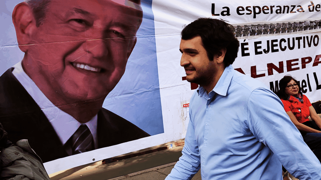 Andrés Manuel López Beltrán camina frente a una lona con el rostro de AMLO durante una campaña política