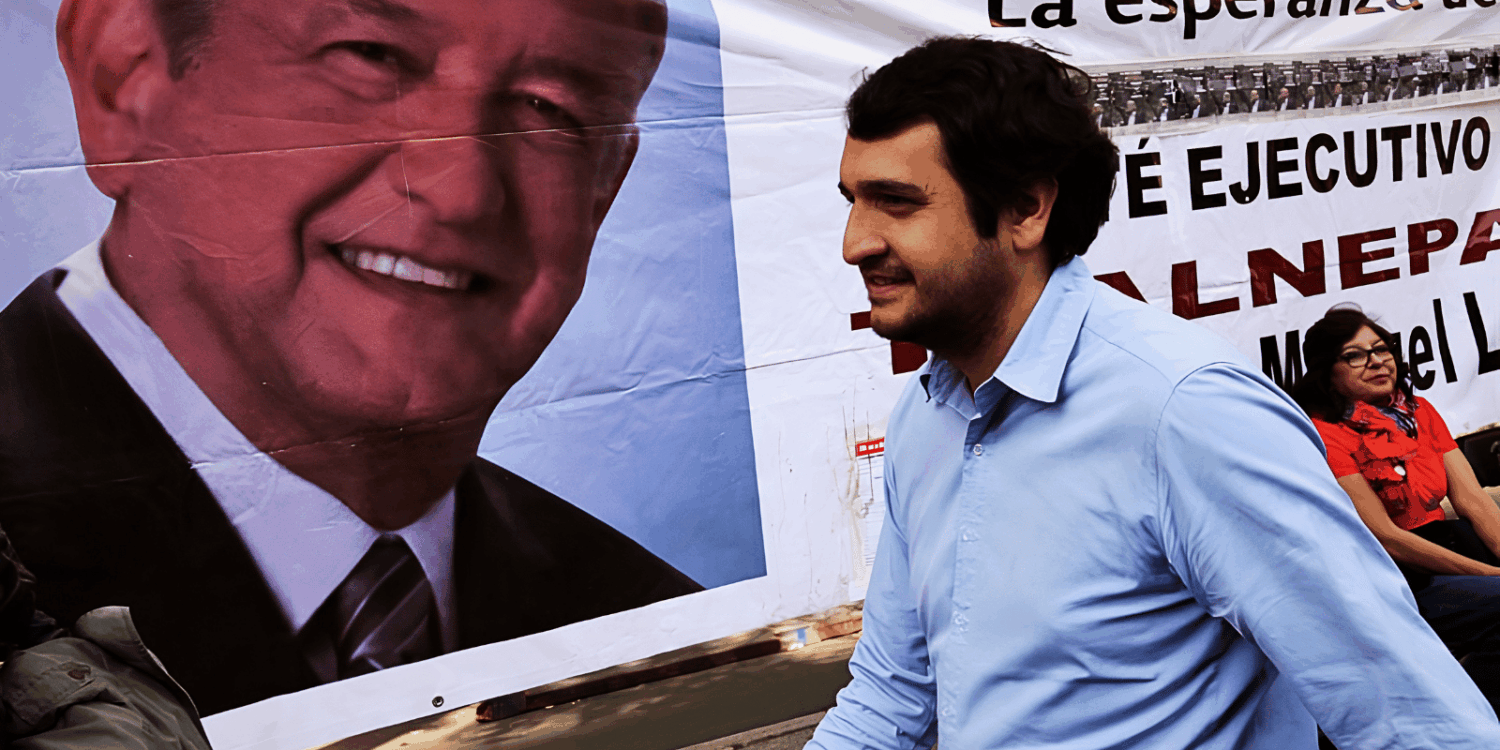 Andrés Manuel López Beltrán camina frente a una lona con el rostro de AMLO durante una campaña política