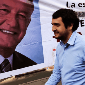 Andrés Manuel López Beltrán camina frente a una lona con el rostro de AMLO durante una campaña política