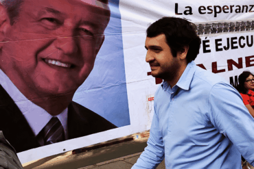 Andrés Manuel López Beltrán camina frente a una lona con el rostro de AMLO durante una campaña política