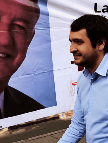 Andrés Manuel López Beltrán camina frente a una lona con el rostro de AMLO durante una campaña política