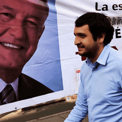 Andrés Manuel López Beltrán camina frente a una lona con el rostro de AMLO durante una campaña política