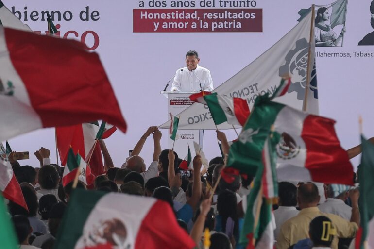 Gobernador Javier May Rodríguez en el podio de la rendición de cuentas de Claudia Sheinbaum en Plaza de Armas de Villahermosa, rodeado de banderas mexicanas