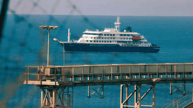 El crucero MV Hondius fondeado frente al puerto industrial de Granadilla en Tenerife, visto a través del alambrado del perímetro de seguridad sanitaria, este sábado previo al desembarco internacional.