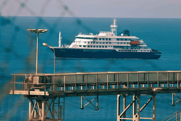 El crucero MV Hondius fondeado frente al puerto industrial de Granadilla en Tenerife, visto a través del alambrado del perímetro de seguridad sanitaria, este sábado previo al desembarco internacional.