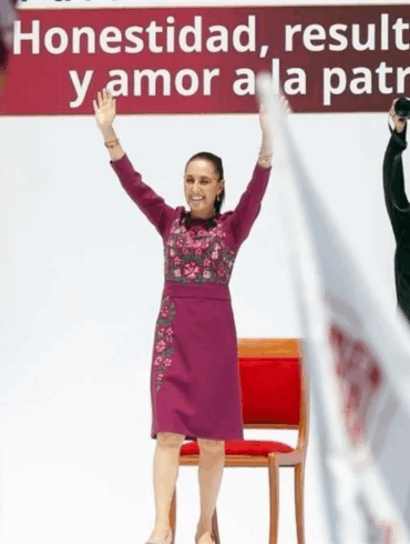 La presidenta Claudia Sheinbaum con los brazos en alto frente al lema Honestidad, resultados y amor a la patria durante su segundo informe de rendición de cuentas en el Monumento a la Revolución