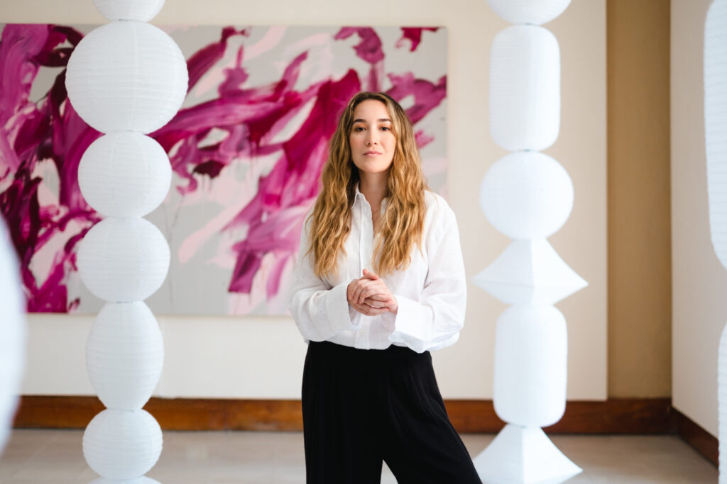 Alejandra Cámara Martínez, nueva subsecretaria de Obras Públicas de Tabasco, fotografiada en galería junto a una de sus pinturas abstractas y una instalación escultórica de esferas blancas.