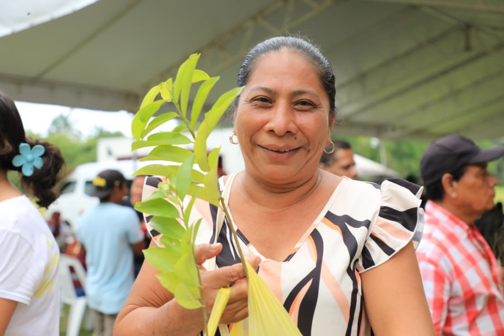 Mujer beneficiaria sostiene una planta durante entrega de apoyos sociales en Paraíso, Tabasco.