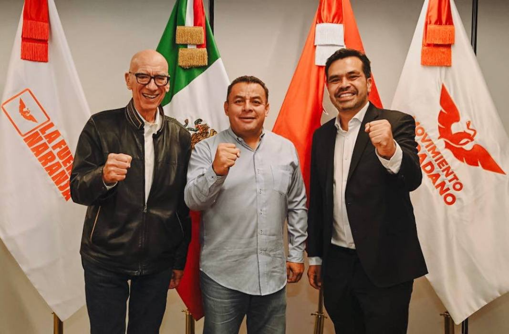 Dante Delgado y Jorge Álvarez Máynez dan la bienvenida a Erubiel Alonso en las oficinas nacionales de Movimiento Ciudadano. Los tres posan con el puño en alto frente a banderas de MC y la bandera de México.